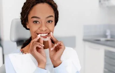 patient smiling while holding her Invisalign clear aligners