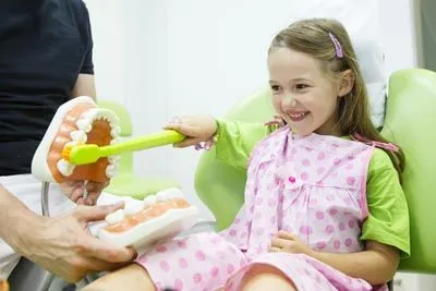 young patient brushing a model of teeth with a large toothbrush